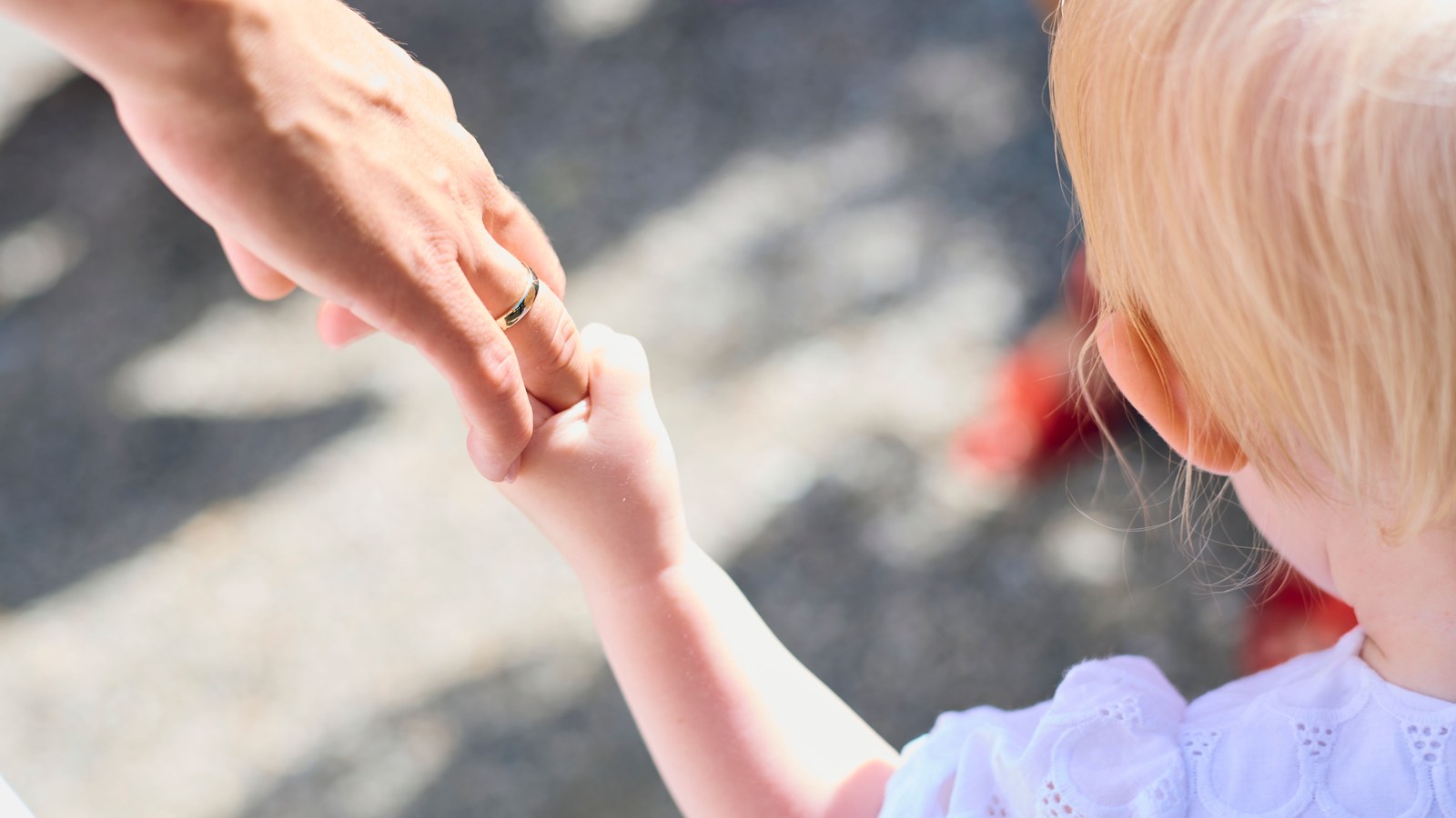 A close view of an adult's hand gently guiding a young child's hand, showing an early tactile communication moment.