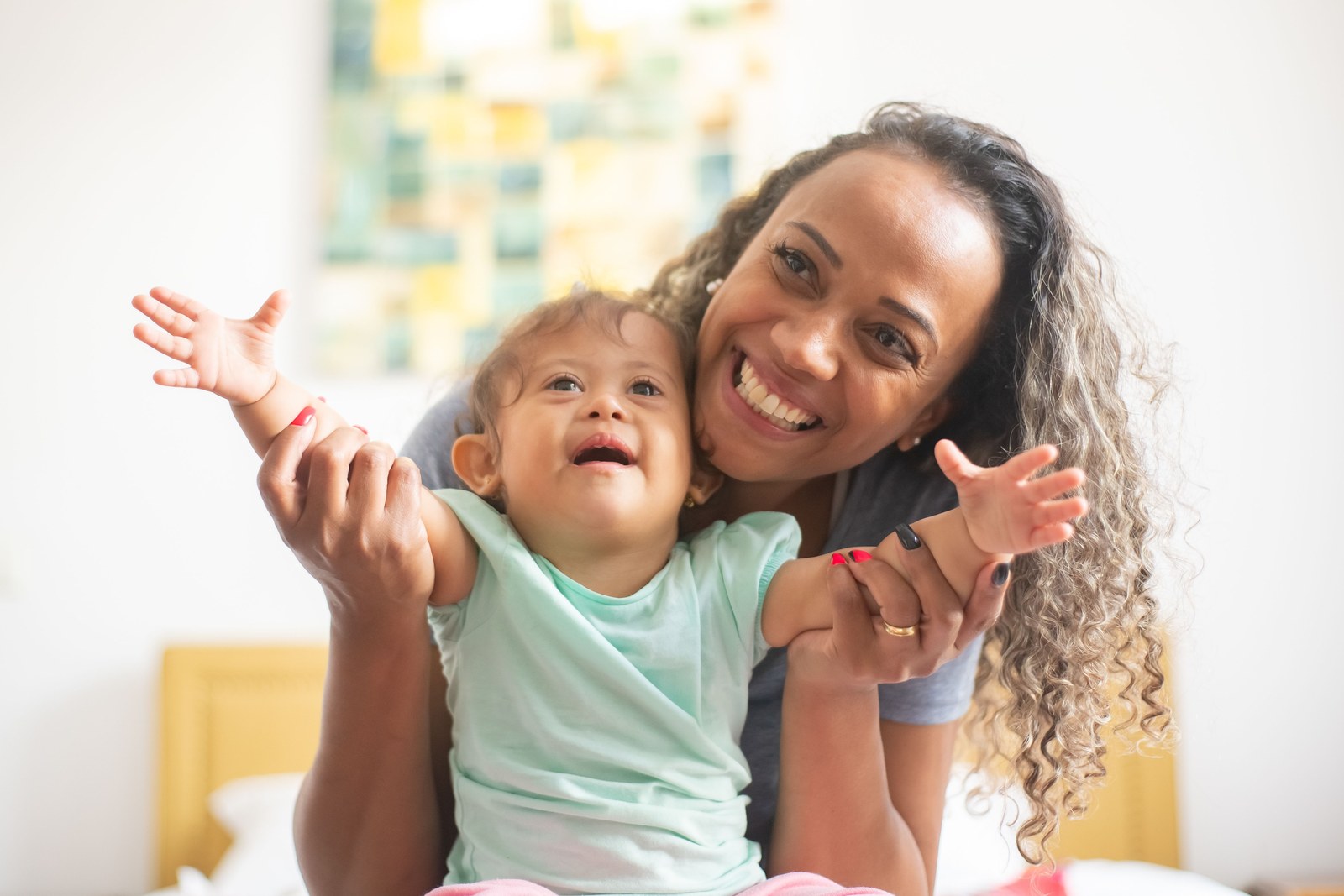 A mother and young child smiling and reaching out together at home.